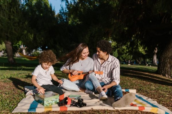 A joyful family enjoying a summer picnic with a ukulele in a sunny park setting.